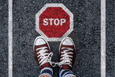 zwei Füße in roten Sneakern von oben, die auf Asphalt stehen, wo ein Stopschild aufgedruckt ist
