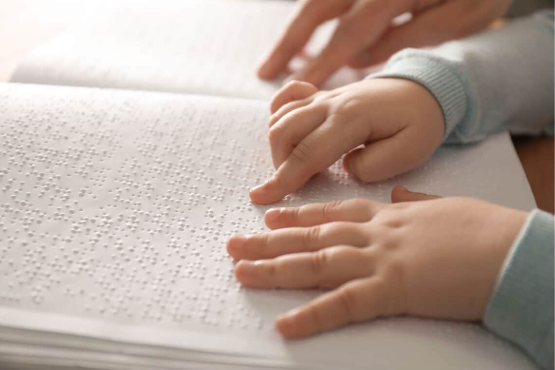 Kinderhände, die in einem Buch Braille lesen