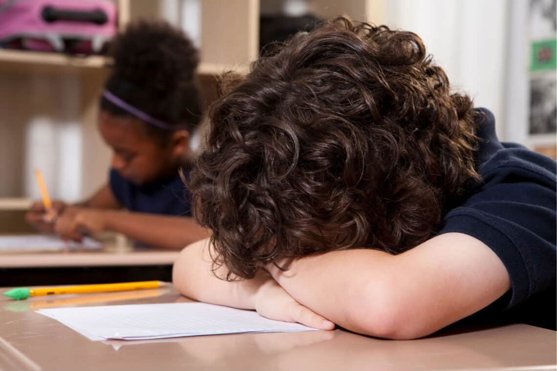 Kind in der Schule, das den Kopf auf die Tischplatte gelegt hat