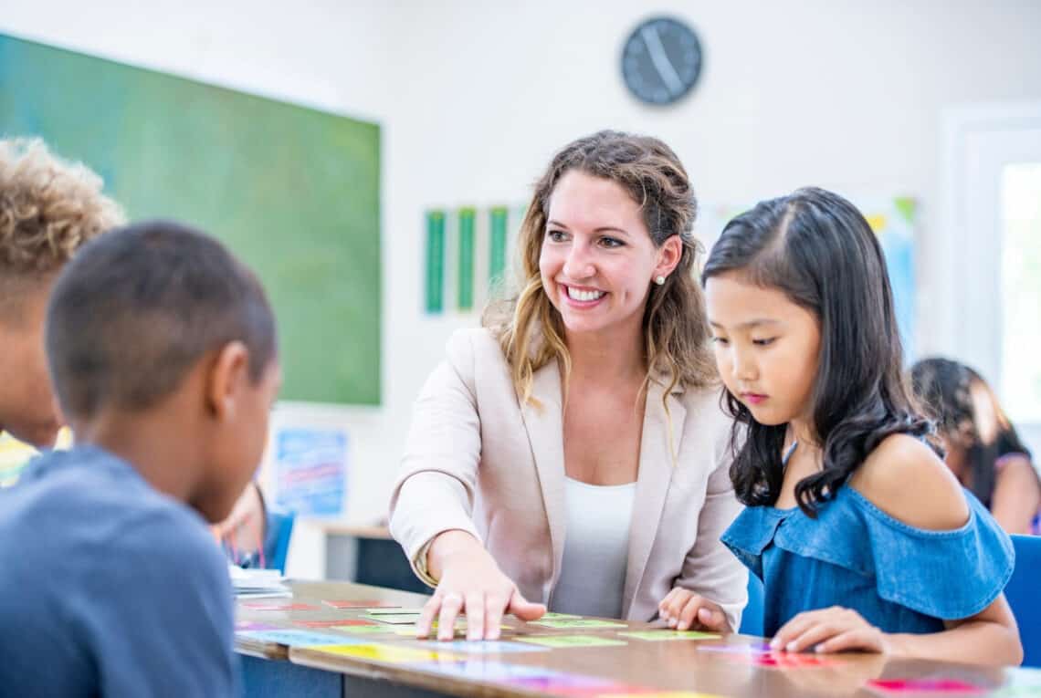 Lehrerin mit einer Gruppe Schüler*innen an einem Tisch mit bunten Kärtchen