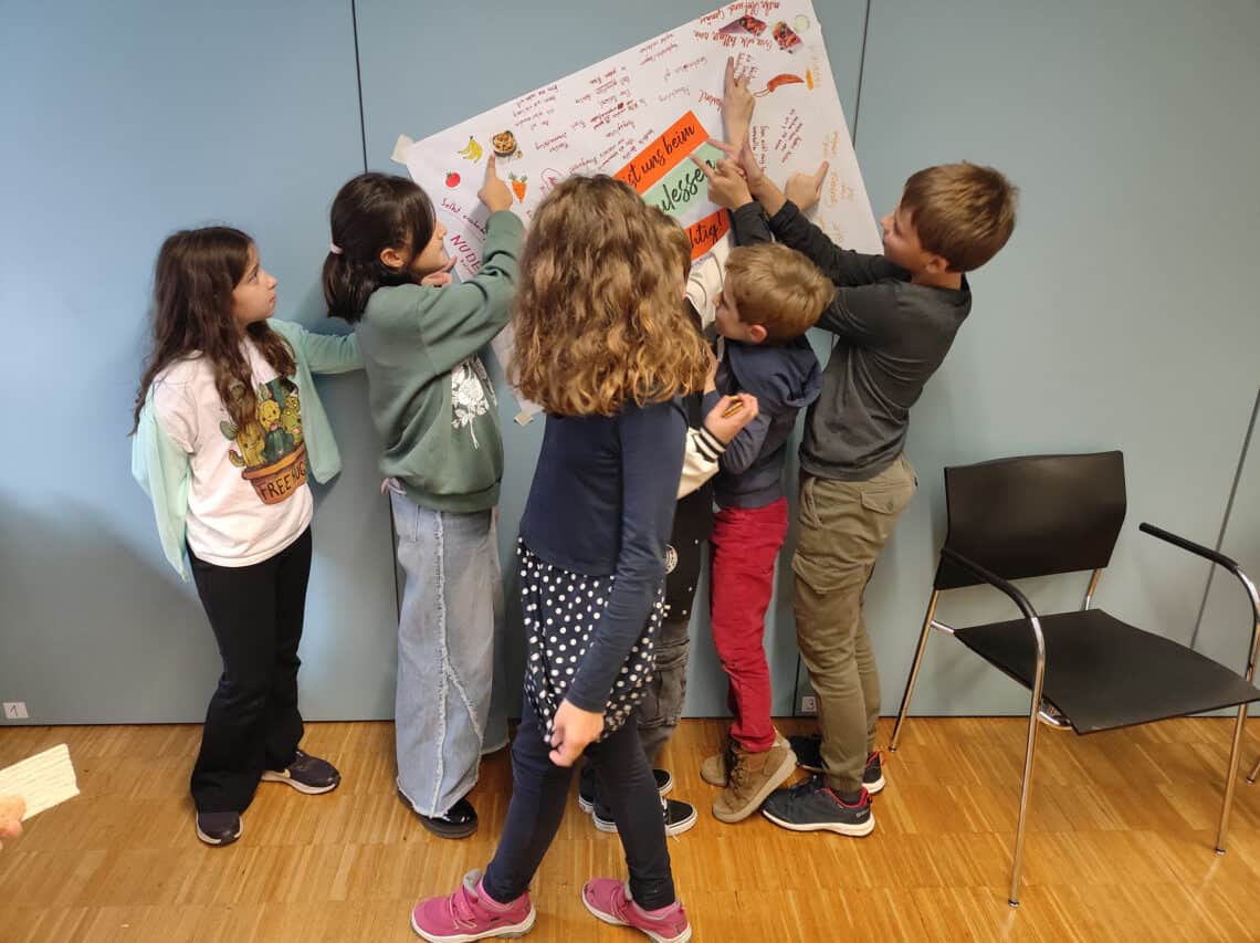 5 Kinder hängen an einer Wand ein Plakat auf