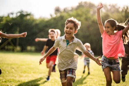 eine Gruppe Kinder, die im Sonnenschein über eine Wiese läuft