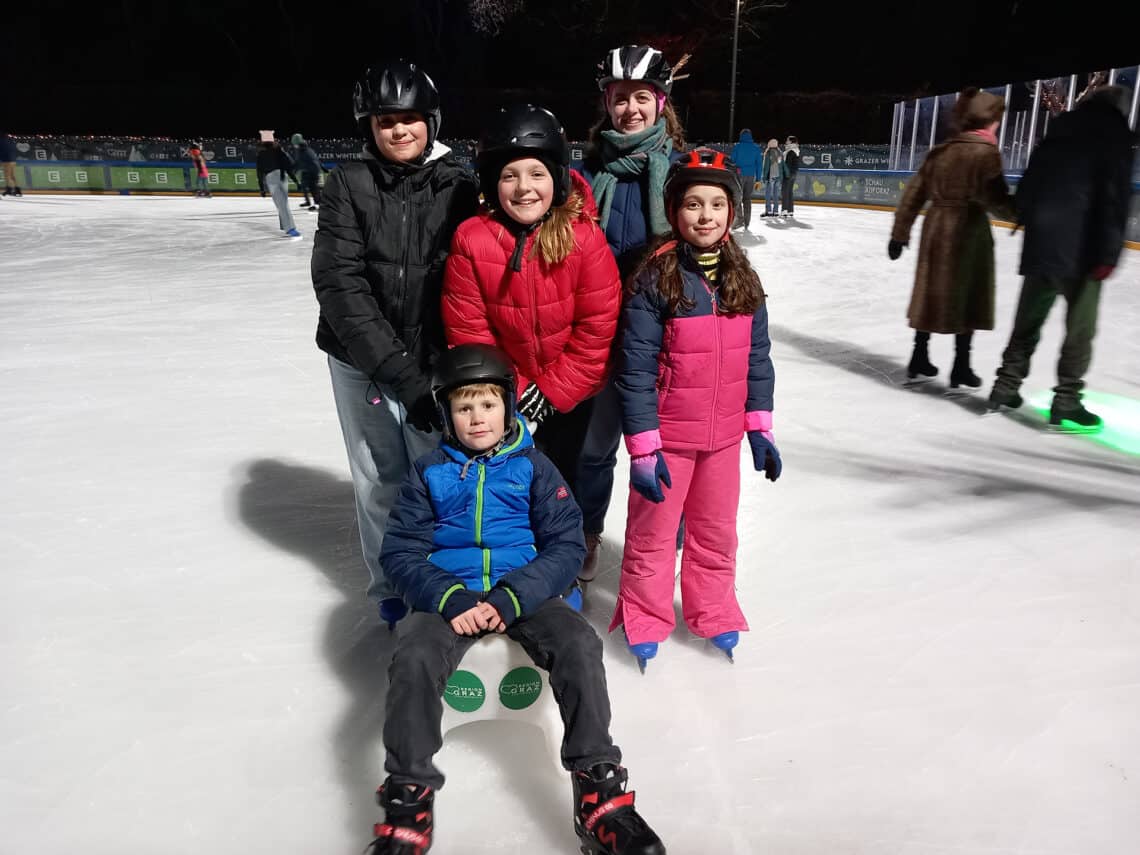 4 Kinder und eine Frau posieren auf einem Eislaufplatz